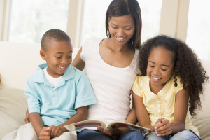 Woman and two children sitting in living room reading book and s